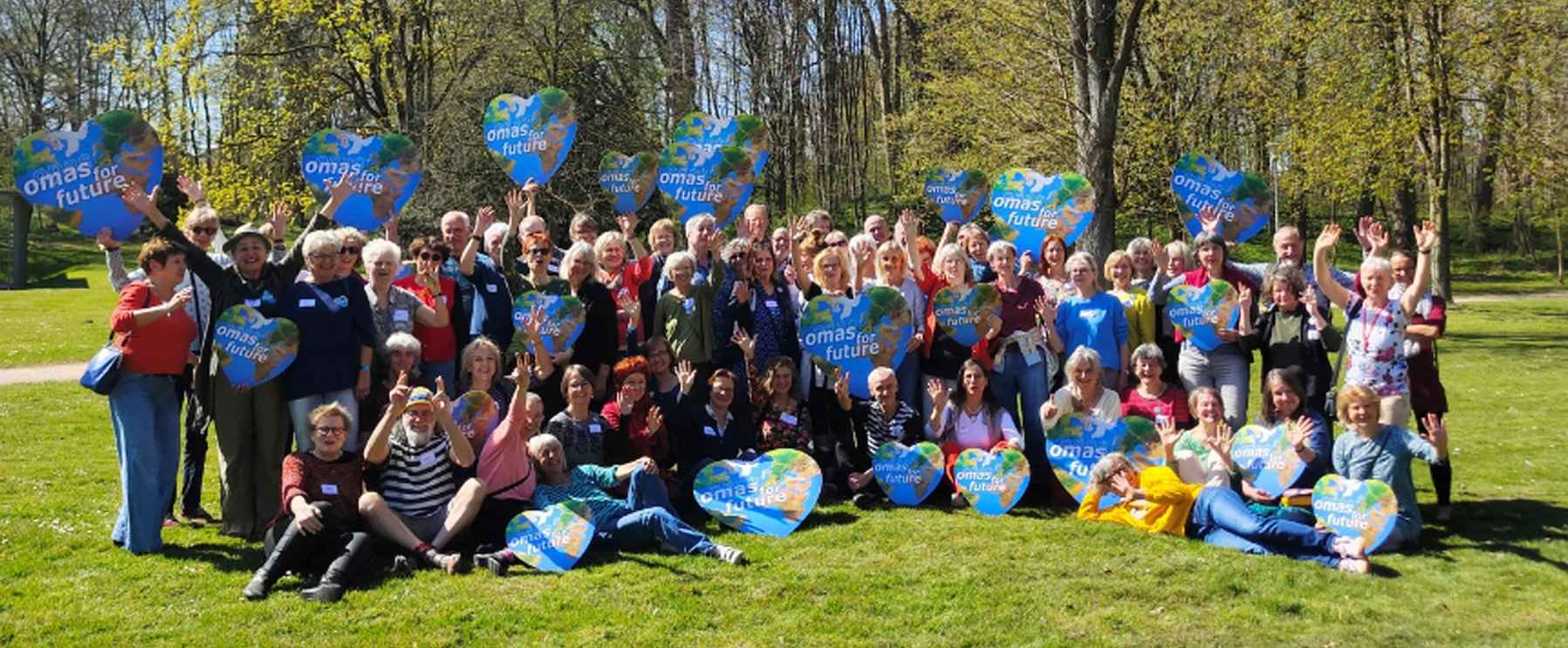 Großes Gruppenbild mit Mitglidern von Omas for Future. Ein paar halten Herzen mit dem Logo der Organisation in der Hand.
