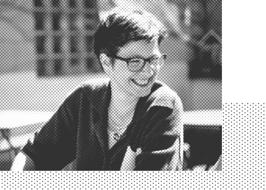 Schwarz-Weiß-Bild einer Frau mit kurzen Haaren und Brille, die lächelt und dabei zur Seite schaut und im Freien sitzt.