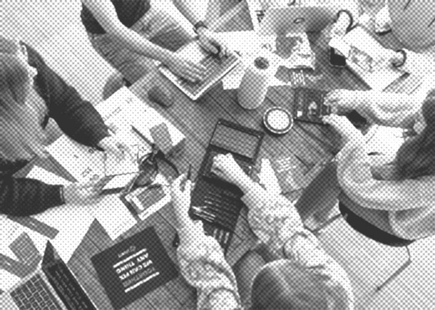 Fünf Personen sitzen mit Laptops, Papieren und Tablets um einen Tisch und arbeiten zusammen.