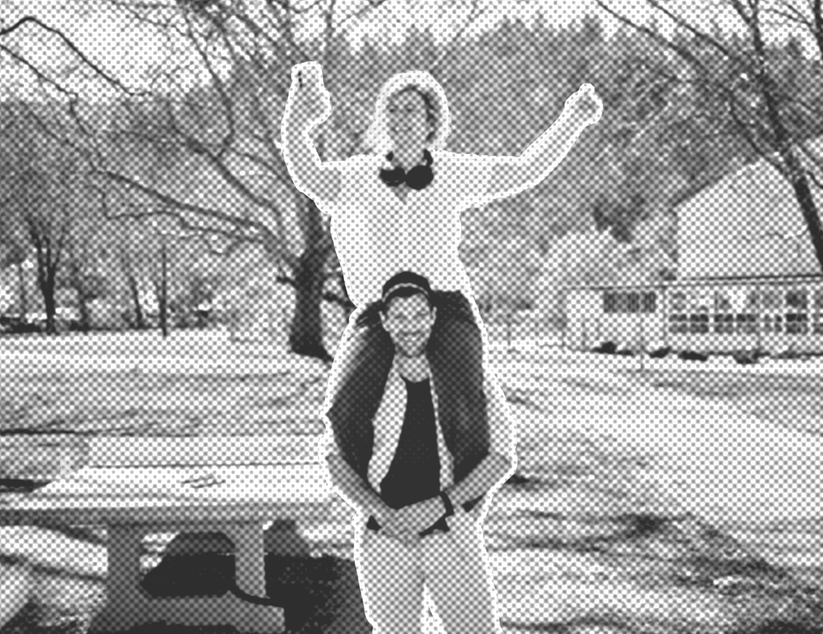 Mann trägt Frau Huckepack. Die Frau hält ihr Handy in der Hand