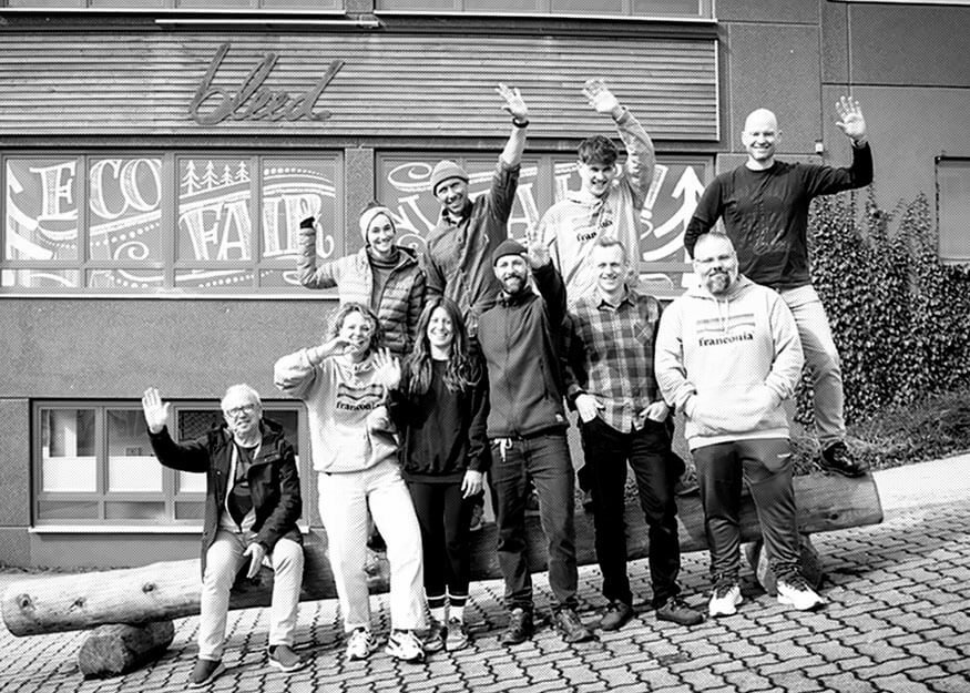 Eine Gruppe von Menschen posiert und winkt vor einem Gebäude mit Graffiti-Kunst.