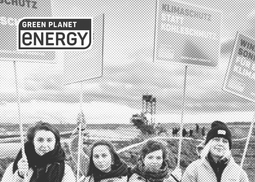 Vier Personen in Winterkleidung halten Protestschilder. Im Hintergrund sind ein Braunkohlebagger und ein bewölkter Himmel zu sehen. In der oberen linken Ecke ist ein „Green Planet Energy“-Logo zu sehen.