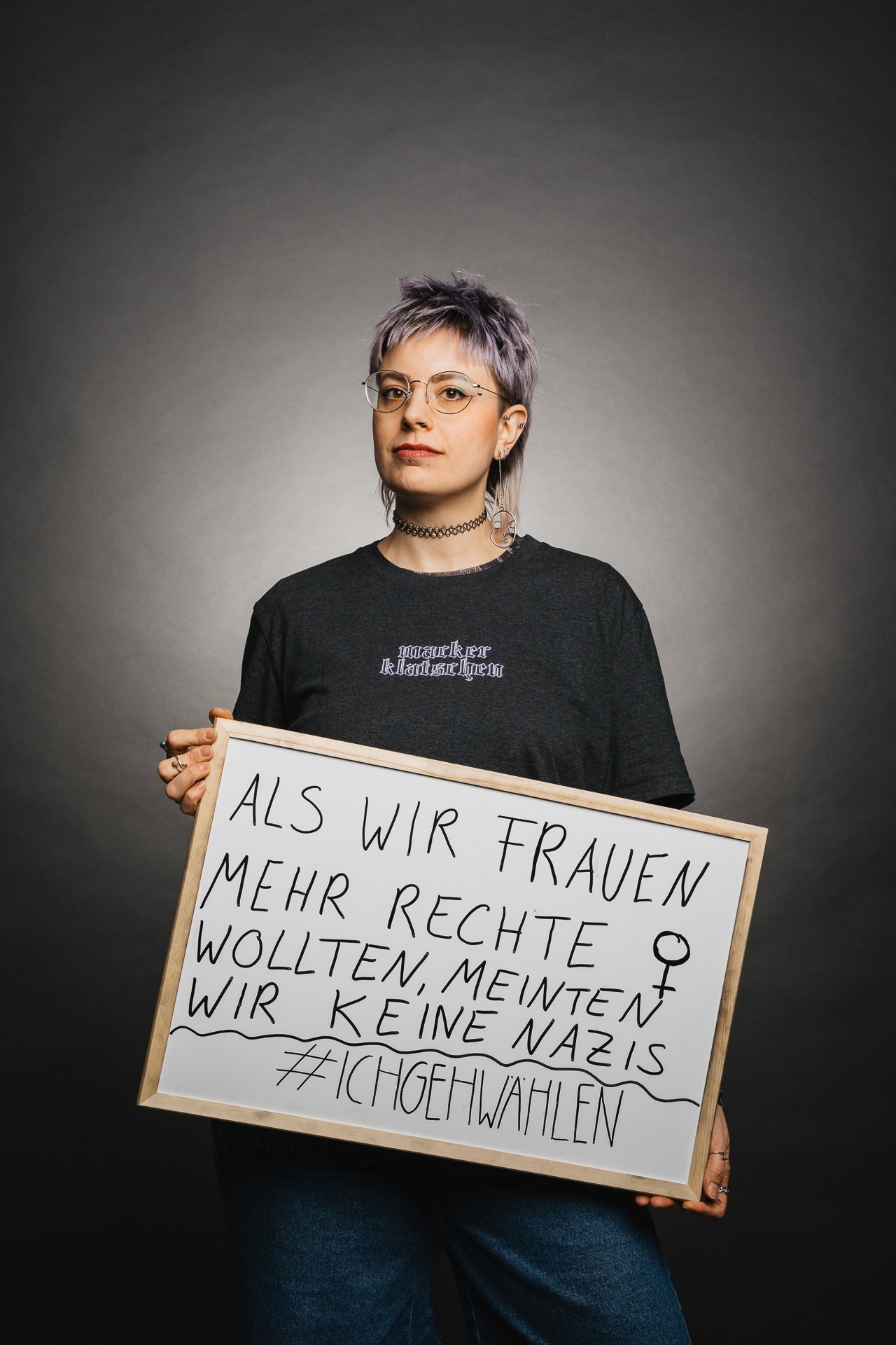 Person mit Brille, die ein Schild mit der Aufschrift „Als wir Frauen mehr Rechte wollten, meinten wir keine Nazis“ hält.