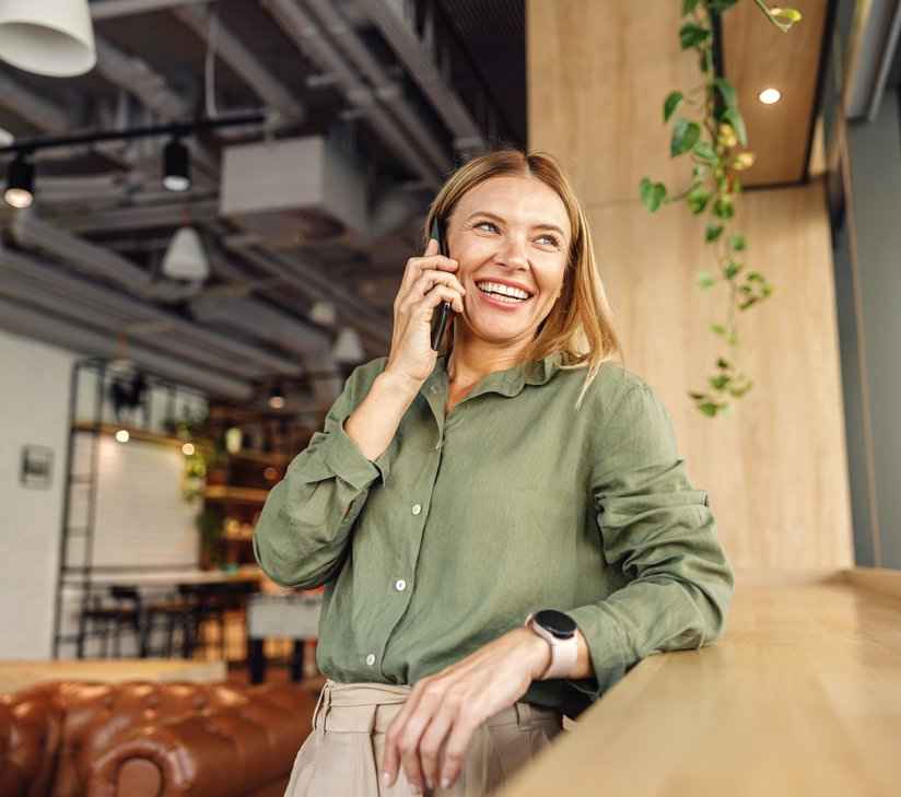 Eine Geschäftsfrau in einem Coworking-Büro telefoniert mit einem Smartphone vor einem Fenster.