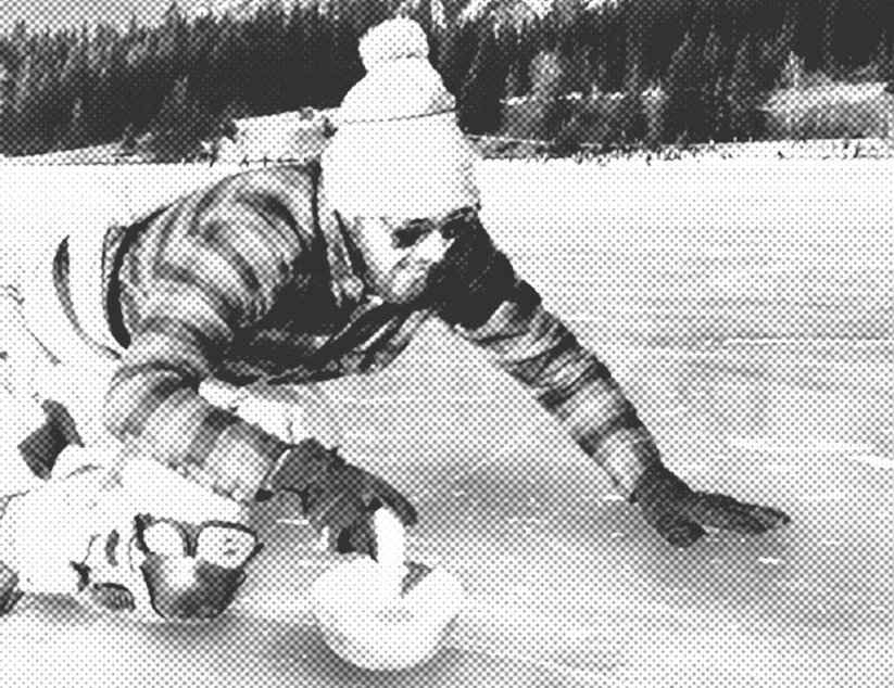 Ein Mann in Winterkleidung kniet auf einem zugefrorenen See und schiebt einen Curlingstein nach vorne.