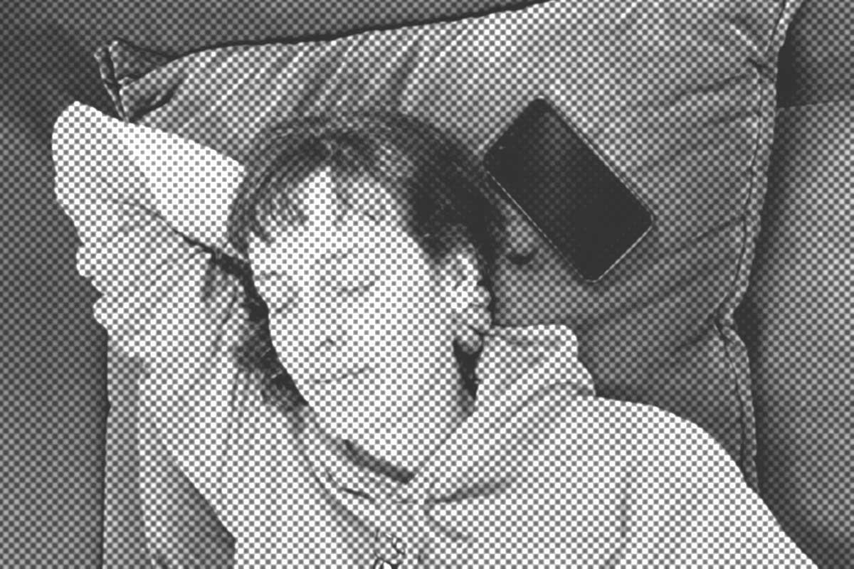 Person mit Kapuzenpullover, die auf einem Kissen schläft und neben sich ein Telefon hat.