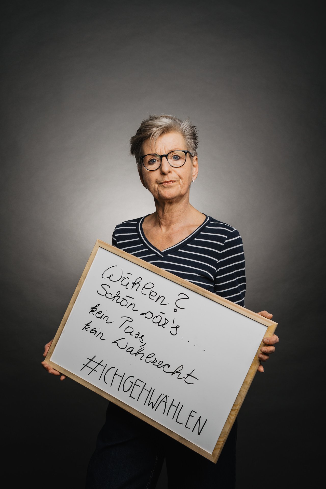 Eine Person mit kurzen grauen Haaren und Brille hält ein Schild mit einem handgeschriebenen Text auf Deutsch zur Unterstützung des Wahlrechts.