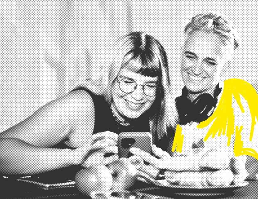 Zwei Frauen schauen gut gelaunt zusammen in ein Handy, das eine von ihnen in der Hand hält.