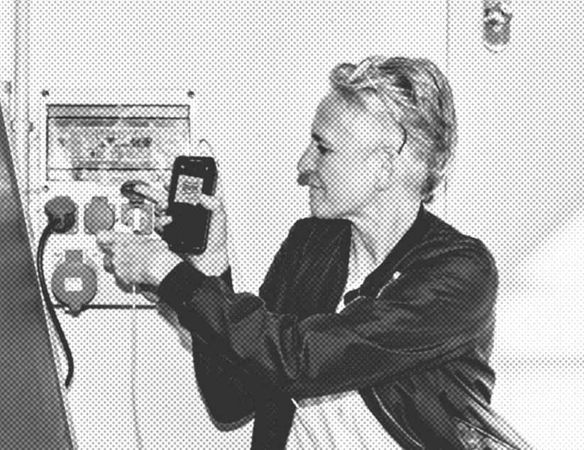 Eine Frau mit kurzen Haaren steckt das Ladekabel ihres Handys in eine Mehrfachsteckdose an der Wand.