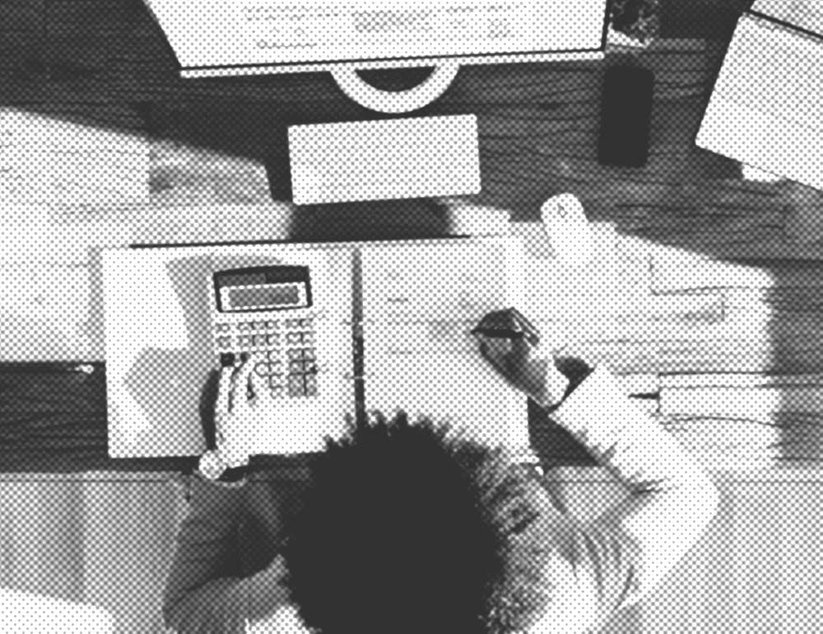Eine Person berechnet Zahlen auf einem Taschenrechner an einem Schreibtisch, umgeben von Notizbüchern und einem Computermonitor in einer Draufsicht.