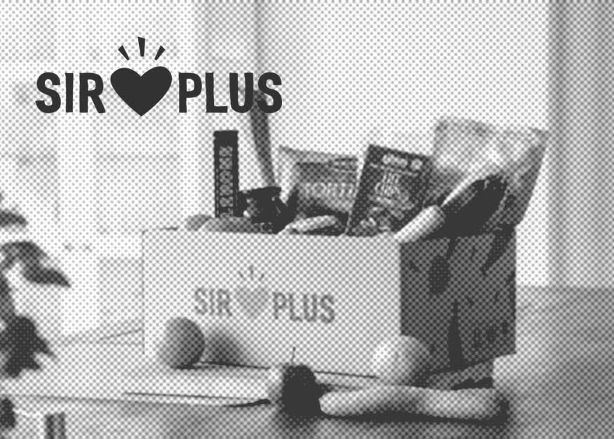 Eine Schachtel mit verschiedenen abgepackten Lebensmitteln auf einem Tisch, mit der Aufschrift „Sir Plus“ und einem Herzsymbol.