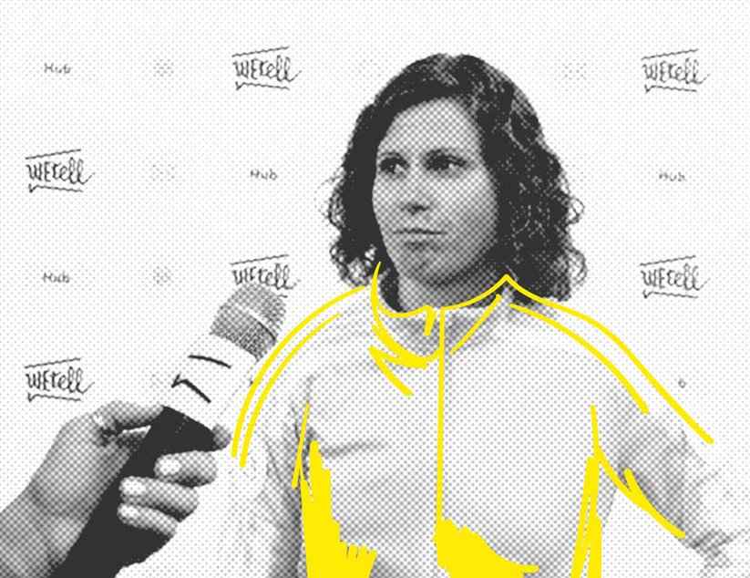 Einer Frau im Trainingsanzug wird ein Mikrofon hingehalten. Im Hintergrund ist eine Wand zu sehen, auf der "WEtell Hub" steht.