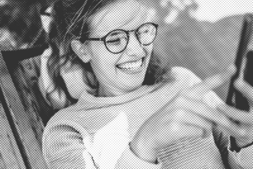 Newsblog, Eine lachende junge Frau mit Brille liegt auf einem Liegestuhl und schaut auf ihr Smartphone.