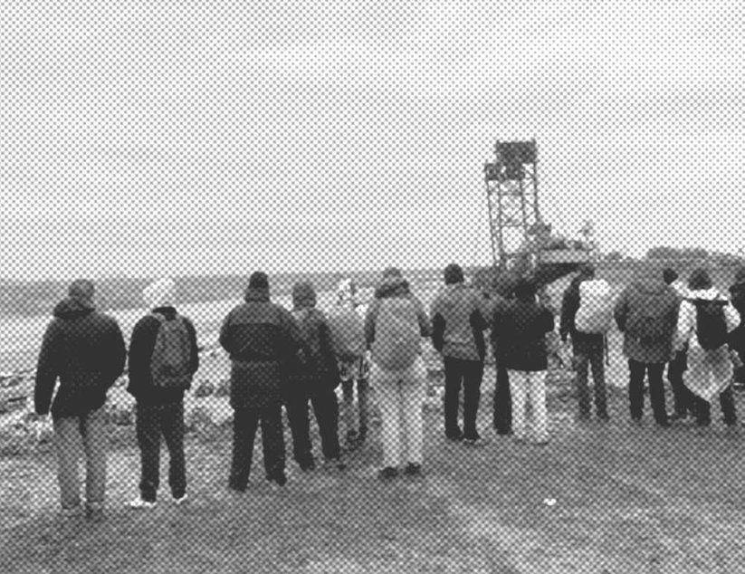 Eine Gruppe von Menschen steht auf dem Gras und blickt unter einem bewölkten Himmel auf ein großes Braunkohleaubbaugebiet.