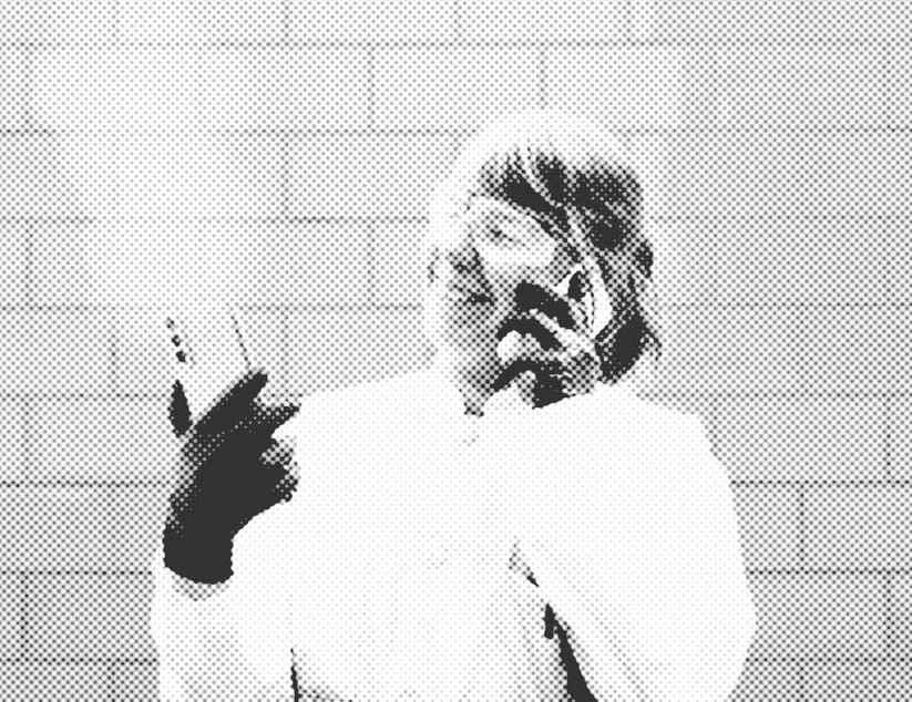 Eine Frau im Laborkittel mit Handschuhen und Sicherheitsbrille schaut sich ein Handy an, während sie mit einem zweiten Handy telefoniert.