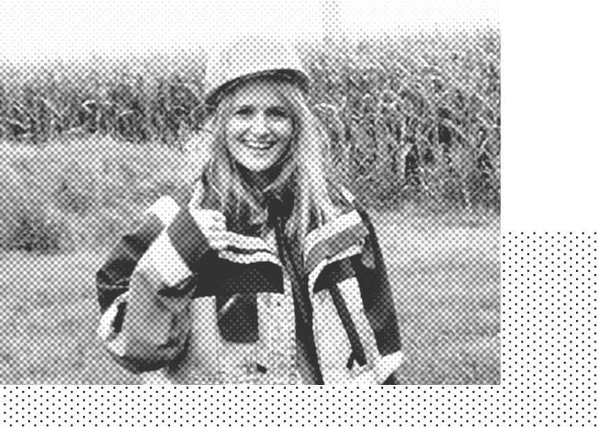Lächelnde Person in Schutzausrüstung und Bauhelm mit einem Maisfeld im Hintergrund. Schwarzweißbild mit gepunktetem Mustereffekt.