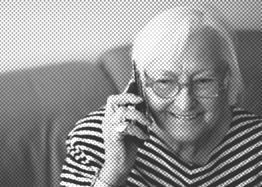 Ältere Person mit Brille und gestreiftem Hemd sitzt lächelnd auf einem Sofa und telefoniert mit dem Handy. Das Bild hat einen Punktmusterfilter.