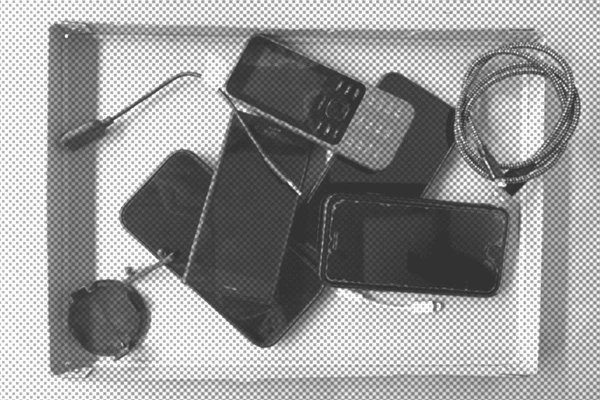 Ein Tablett mit verschiedenen elektronischen Artikeln, darunter mehrere Telefone, ein Ladegerät und ein Spiralkabel, die auf einem Stapel angeordnet sind.