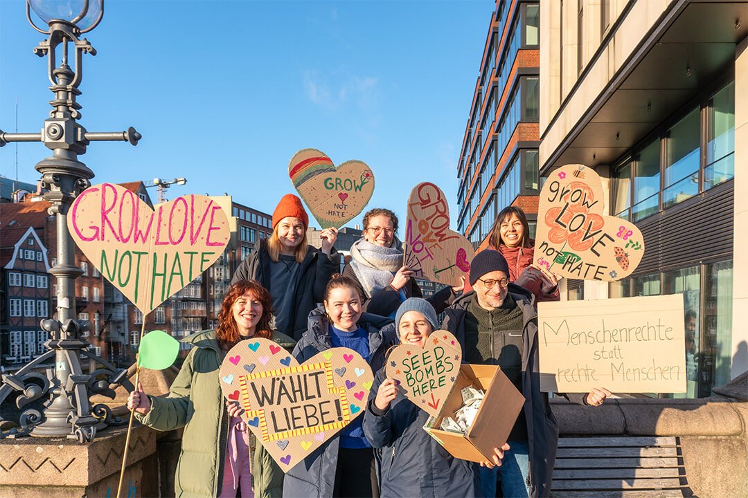 Eine Gruppe von Menschen hält herzförmige Schilder mit Botschaften, die für Liebe und Akzeptanz werben, und steht auf einer Stadtstraße in der Nähe moderner Gebäude.