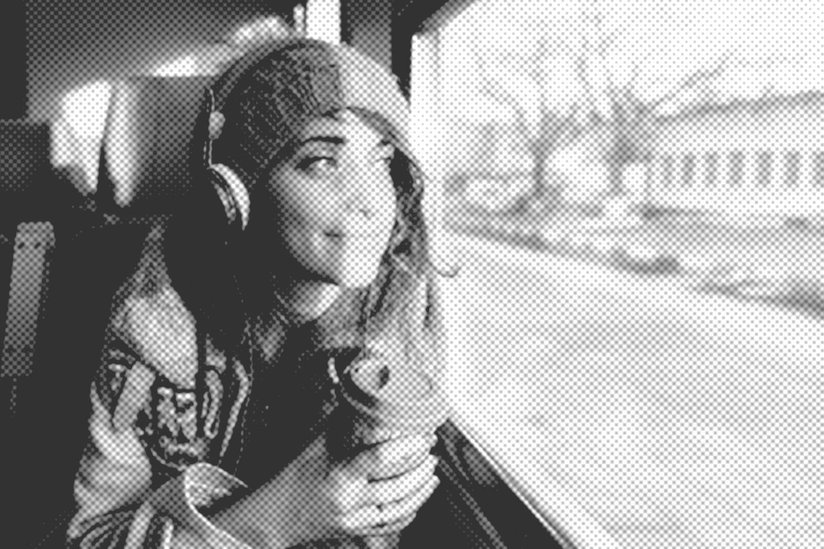Podcast, Eine junge Frau mit Kopfhörern mit einem Kaffeebecher in der Hand sitzt in der Bahn und schaut aus dem Fenster.