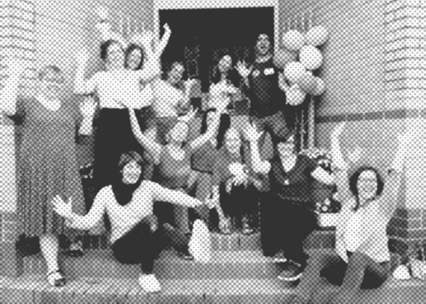 Eine Gruppe von Menschen posiert energisch auf Stufen, einige halten Luftballons in den Händen. Sie scheinen ein Ereignis zu feiern.
