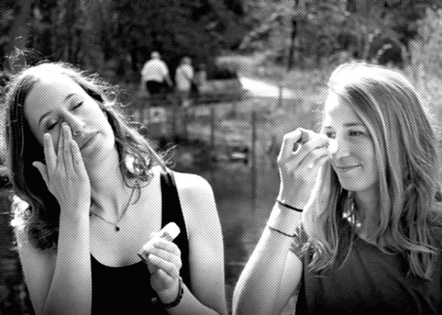 Zwei Frauen tragen im Freien Sonnenschutz auf. Sie stehen neben einem Gewässer. Im Hintergrund sind Bäume zu sehen.