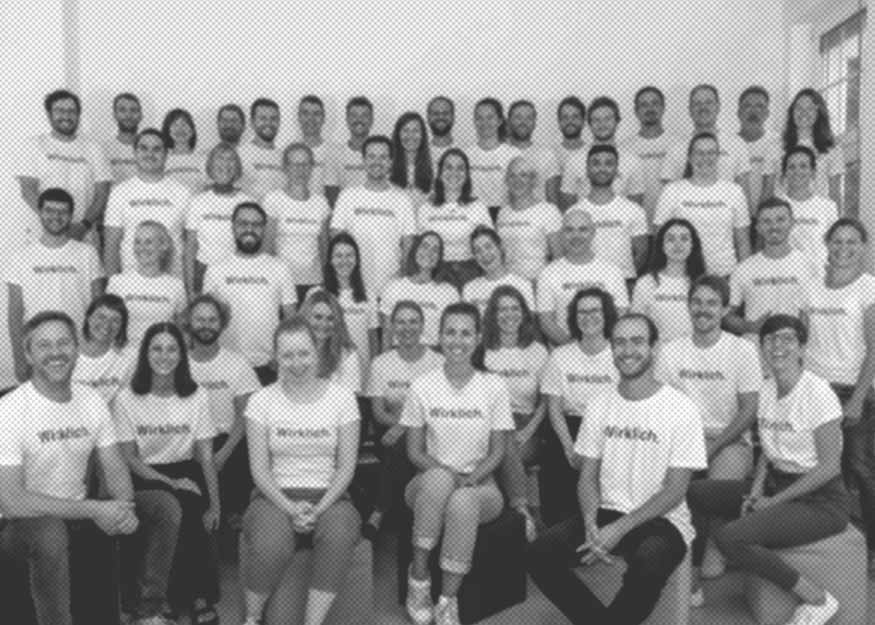 Gruppenfoto von Menschen in passenden Hemden, die in Reihen angeordnet sind und in einem gut beleuchteten Raum in die Kamera lächeln.