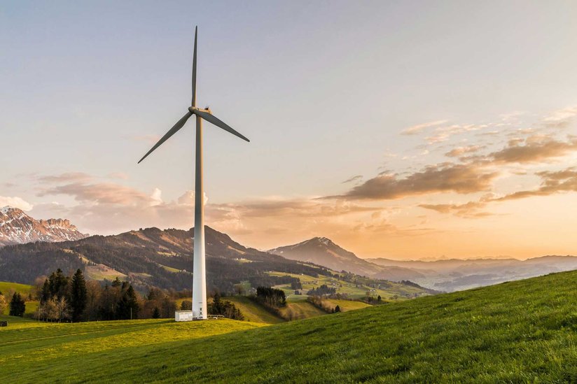 Ein Windrad steht in einer bergigen Landschaft im Sonnenuntergang